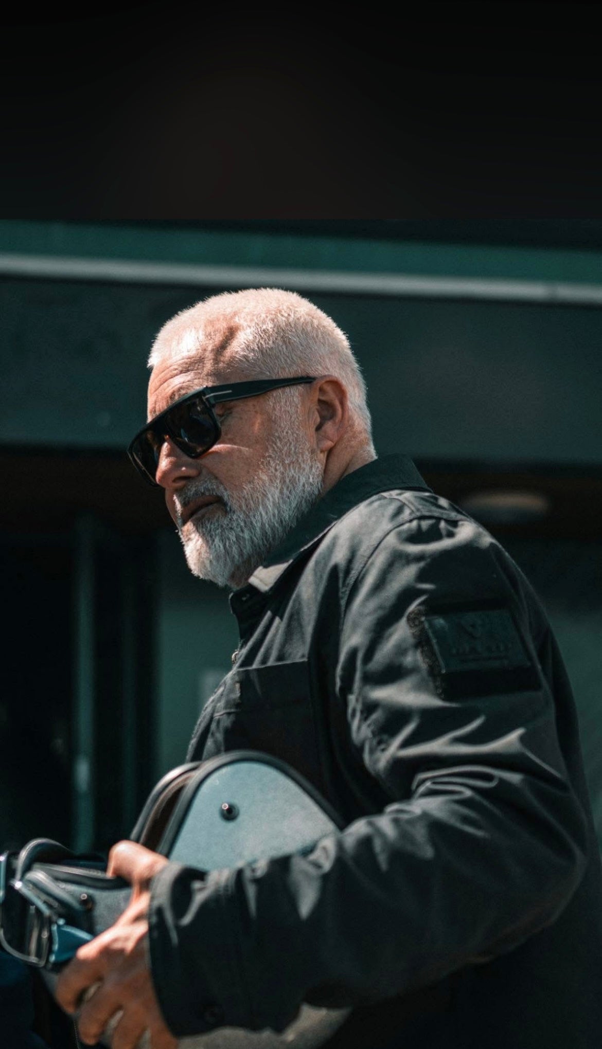Terry Bradley wearing sunglasses in a motorcycle jacket, holding a motorcycle helmet at his One Road event in Belfast